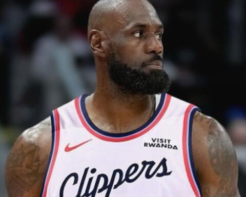 Basketball player in a white Clippers jersey with red and blue trim, looking to the right with a full beard.