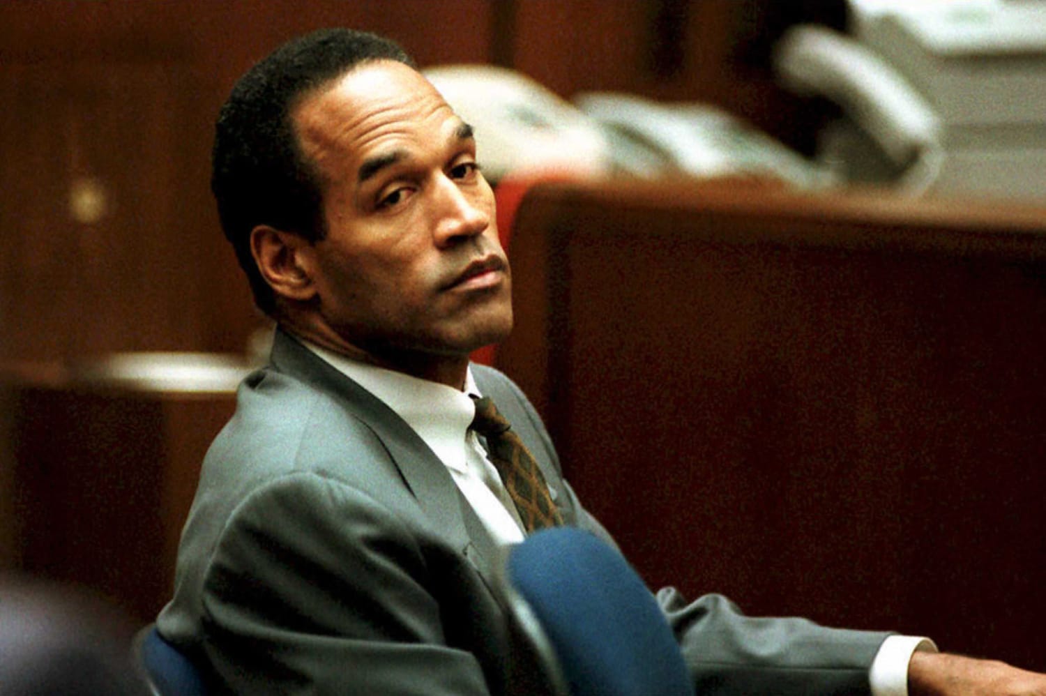 Man in a gray suit seated in a courtroom, looking to the left.