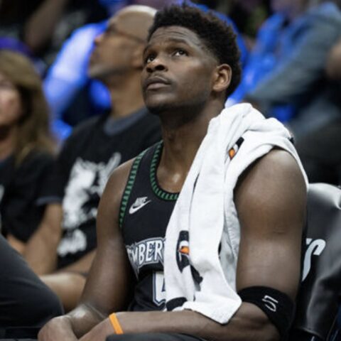 Basketball player sits on a bench with a towel over his shoulder, looking up during a game.