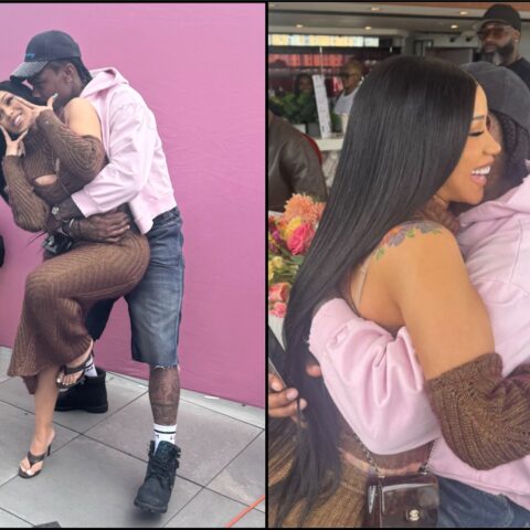 Couple posing affectionately: man in a pink hoodie lifts woman in a brown knit dress against a pink wall, rooftop setting.