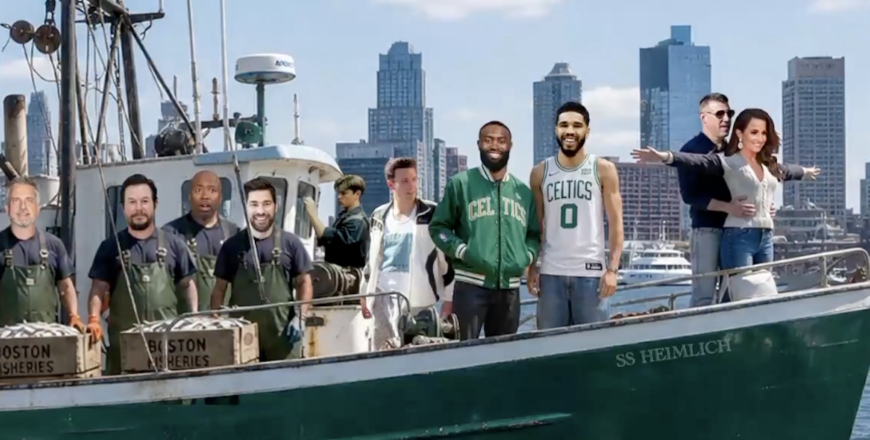 Group of men on a green fishing boat in a harbor, with a city skyline in the background.
