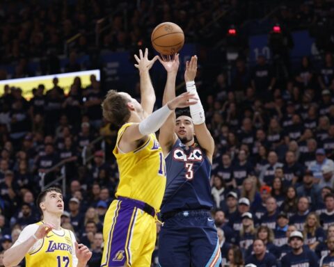 Two basketball players jump for the ball in a crowded arena as fans look on.