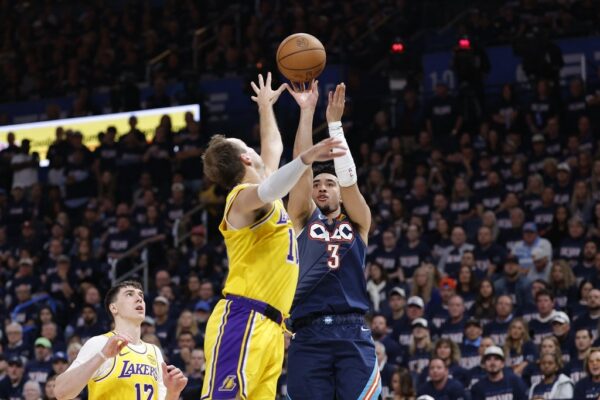 Two basketball players jump for the ball in a crowded arena as fans look on.