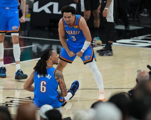 Oklahoma City Thunder players confront each other on the court; one sits on the floor with number 6, the other stands in a ready stance wearing number 3, surrounded by spectators and media.