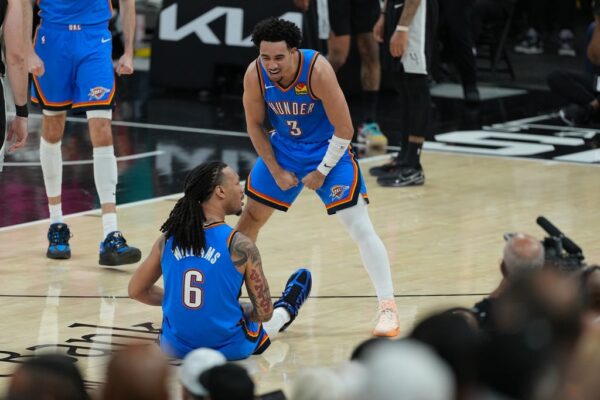 Oklahoma City Thunder players confront each other on the court; one sits on the floor with number 6, the other stands in a ready stance wearing number 3, surrounded by spectators and media.
