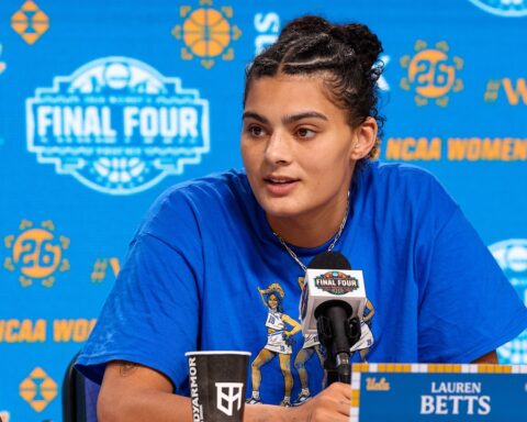 Basketball player Lauren Betts speaks at a press conference microphone with a blue NCAA Final Four backdrop behind her.