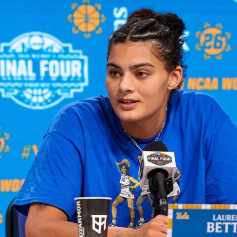 Basketball player Lauren Betts speaks at a press conference microphone with a blue NCAA Final Four backdrop behind her.