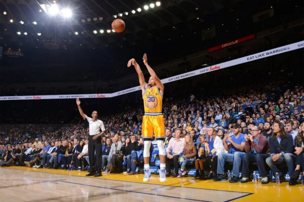 Golden State Warriors player in orange jersey (#30) shooting a jumpshot while crowds watch from the stands.
