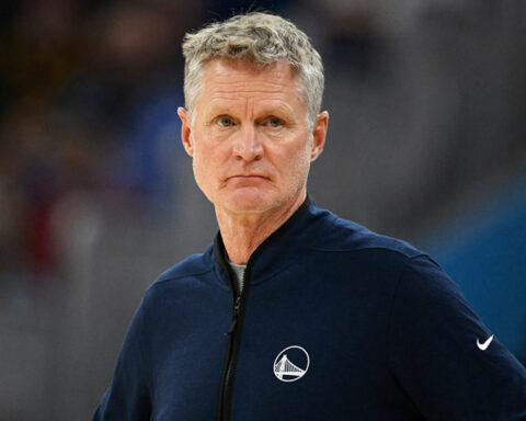 Head-and-shoulders of a man in a navy jacket on a basketball court, looking serious during a game.