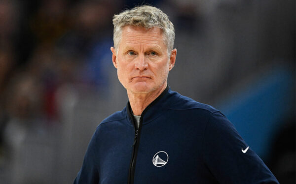 Head-and-shoulders of a man in a navy jacket on a basketball court, looking serious during a game.