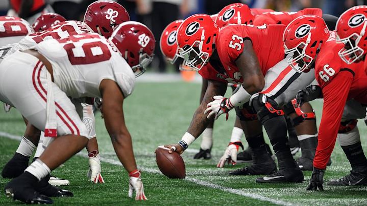 Football players in red and white line up at the snap, ball on the line of scrimmage ready for play intent.