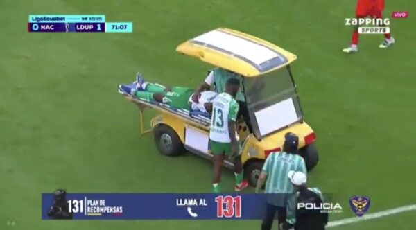 Soccer player in green on a stretcher being loaded into a yellow medical cart on the field, with staff nearby.