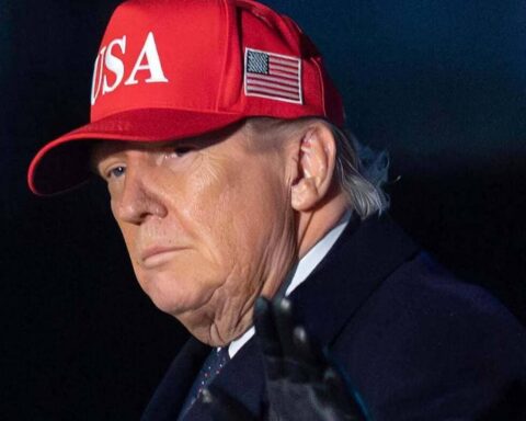 Man wearing a red cap with 'USA' text and an American flag patch, dark coat, looking to the left with a serious expression.