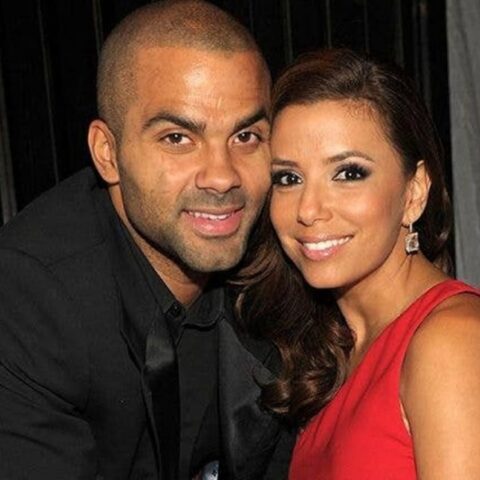 Smiling couple posing closely for a photo at a formal event; man in a black suit and woman in a red dress.