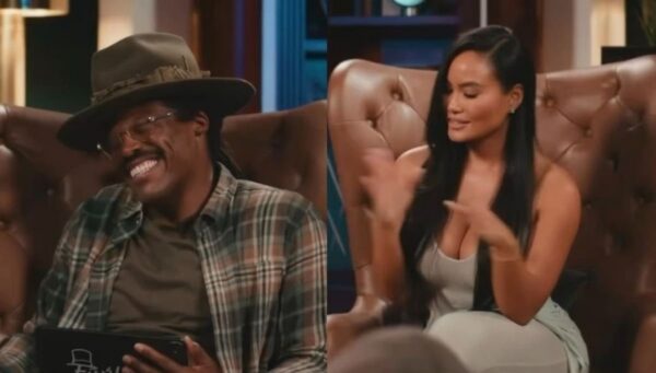 Man wearing a wide hat and plaid shirt laughs while seated on a brown tufted couch; a woman with long black hair sits beside him and gestures as she speaks.
