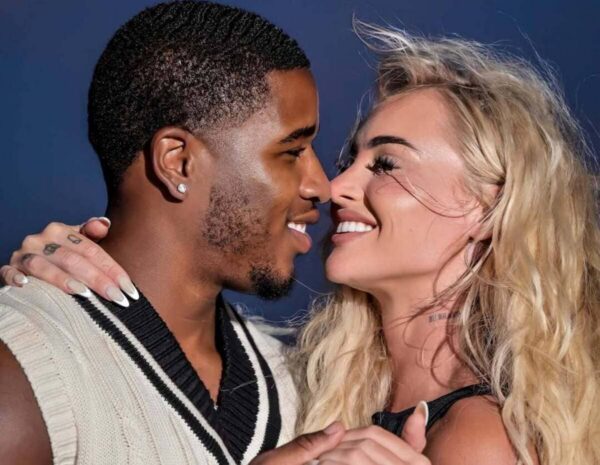 Close-up of a smiling couple nose-to-nose, embracing and looking into each other's eyes against a dark blue background.
