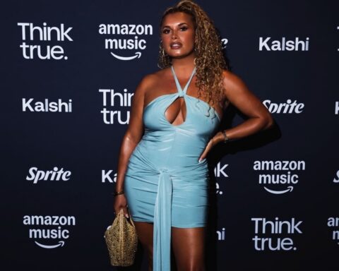 Woman in a light-blue halter mini dress posing on a dark backdrop with sponsor logos.