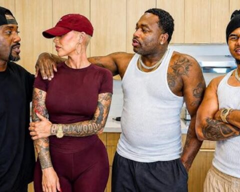 Four friends stand in a kitchen with arms around each other, dressed in casual athletic wear, chatting warmly.