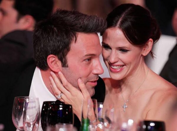 Close-up of a smiling couple at a formal dinner; the woman gently cups the man's face with her hand as they chat.