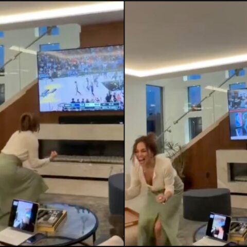 Woman dancing with joy in a modern living room as a basketball game plays on a large TV mounted above a fireplace.