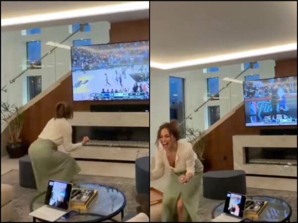 Woman dancing with joy in a modern living room as a basketball game plays on a large TV mounted above a fireplace.