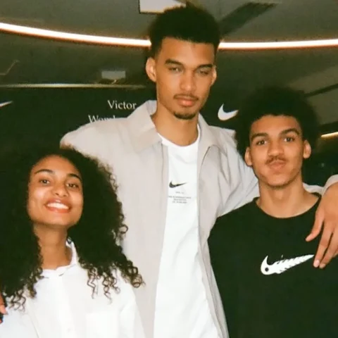 Three young friends posing together with their arms around each other, smiling at the camera, indoors at a Nike event.