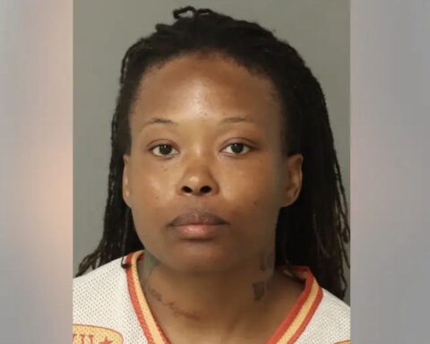 Mugshot of a woman with dreadlocks wearing a white jersey with orange trim, facing the camera with a neutral expression.
