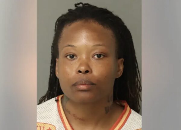 Mugshot of a woman with dreadlocks wearing a white jersey with orange trim, facing the camera with a neutral expression.