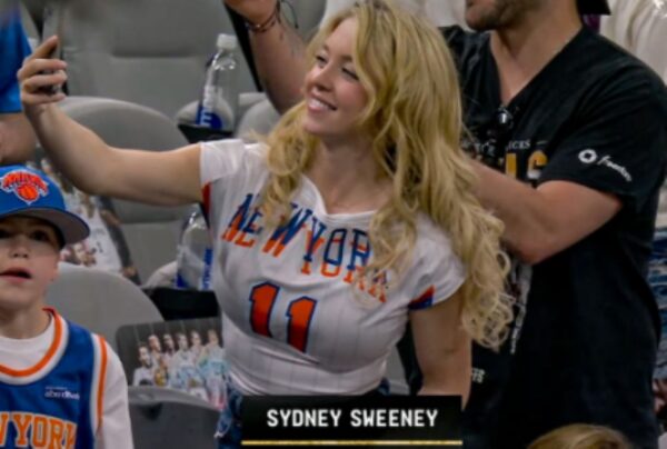 Blonde woman in a New York basketball jersey taking a selfie with a smiling young fan at a game.