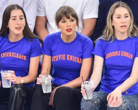 Three women in blue T-shirts with orange text sit on a bench, each holding a clear drink with a straw.