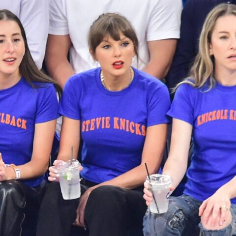 Three women in blue T-shirts with orange text sit on a bench, each holding a clear drink with a straw.