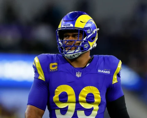 Rams football player wearing a blue and yellow uniform and helmet with captain patch, standing on the field during a game.