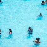 Group of people swimming and playing in bright blue water, with one person holding an orange flotation device.