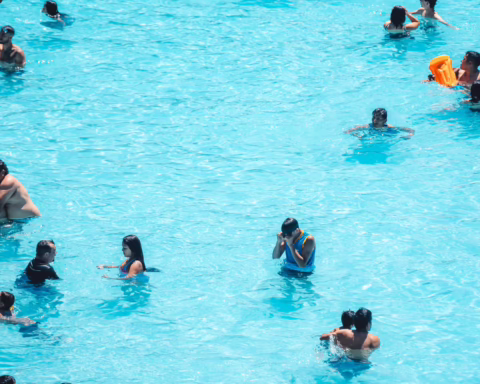 Group of people swimming and playing in bright blue water, with one person holding an orange flotation device.
