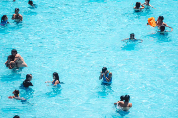 Group of people swimming and playing in bright blue water, with one person holding an orange flotation device.