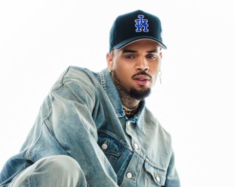 Man wearing a faded blue denim jacket and a black cap with a blue LA logo, posing against a white background.