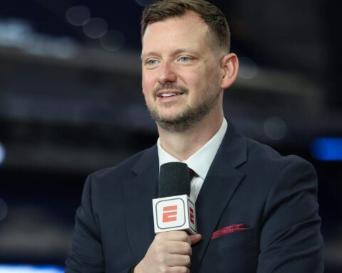 Male sports reporter in a dark suit holds a microphone with an ESPN logo during an interview in a studio setting.