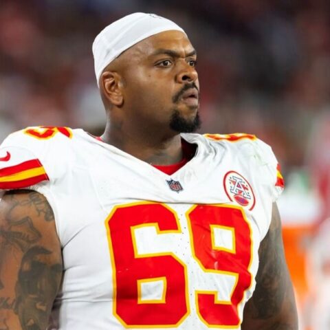 American football player in a white jersey with red and yellow numbers (#69), wearing a white headband, on the field.
