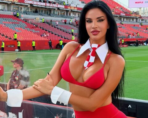 Woman in a red bikini top and white collar with a red-and-white tie posing at a soccer stadium.