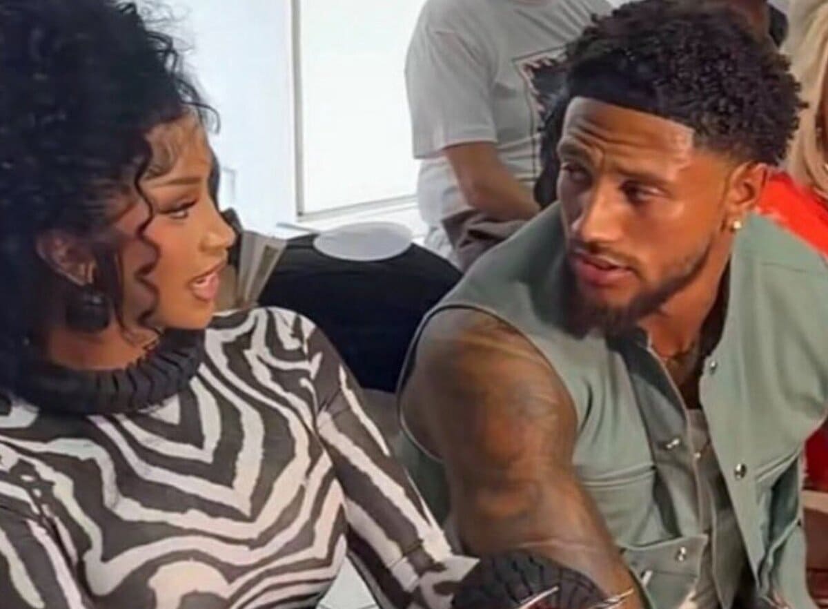 Woman with curly hair in a zebra-print turtleneck talking to a bearded man with tattoos on his arm, seated indoors and looking at each other.