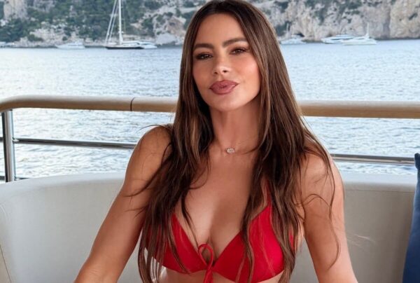 Woman in a red bikini sits on a boat with calm water and rocky coastline in the background.