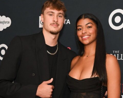 Two people pose together on a red carpet, smiling, with a dark backdrop featuring logos in the background (salesforce, Target). They wear black outfits.