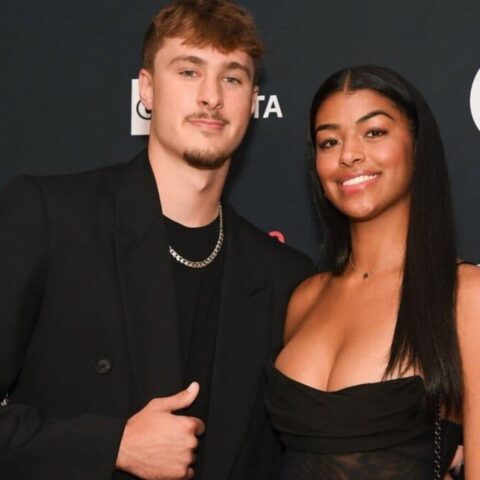 Two people pose together on a red carpet, smiling, with a dark backdrop featuring logos in the background (salesforce, Target). They wear black outfits.