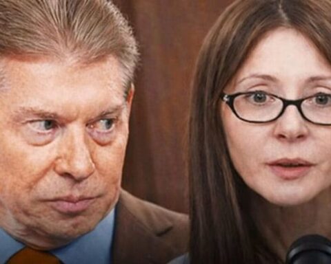 Man and woman in a press conference; the man looks sideways with a tense expression, the woman speaks into a microphone.
