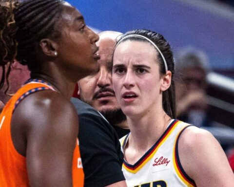 Two female basketball players engage in a tense moment on the court, facing each other with a coach or official between them.