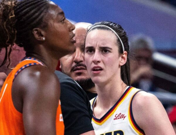 Two female basketball players engage in a tense moment on the court, facing each other with a coach or official between them.
