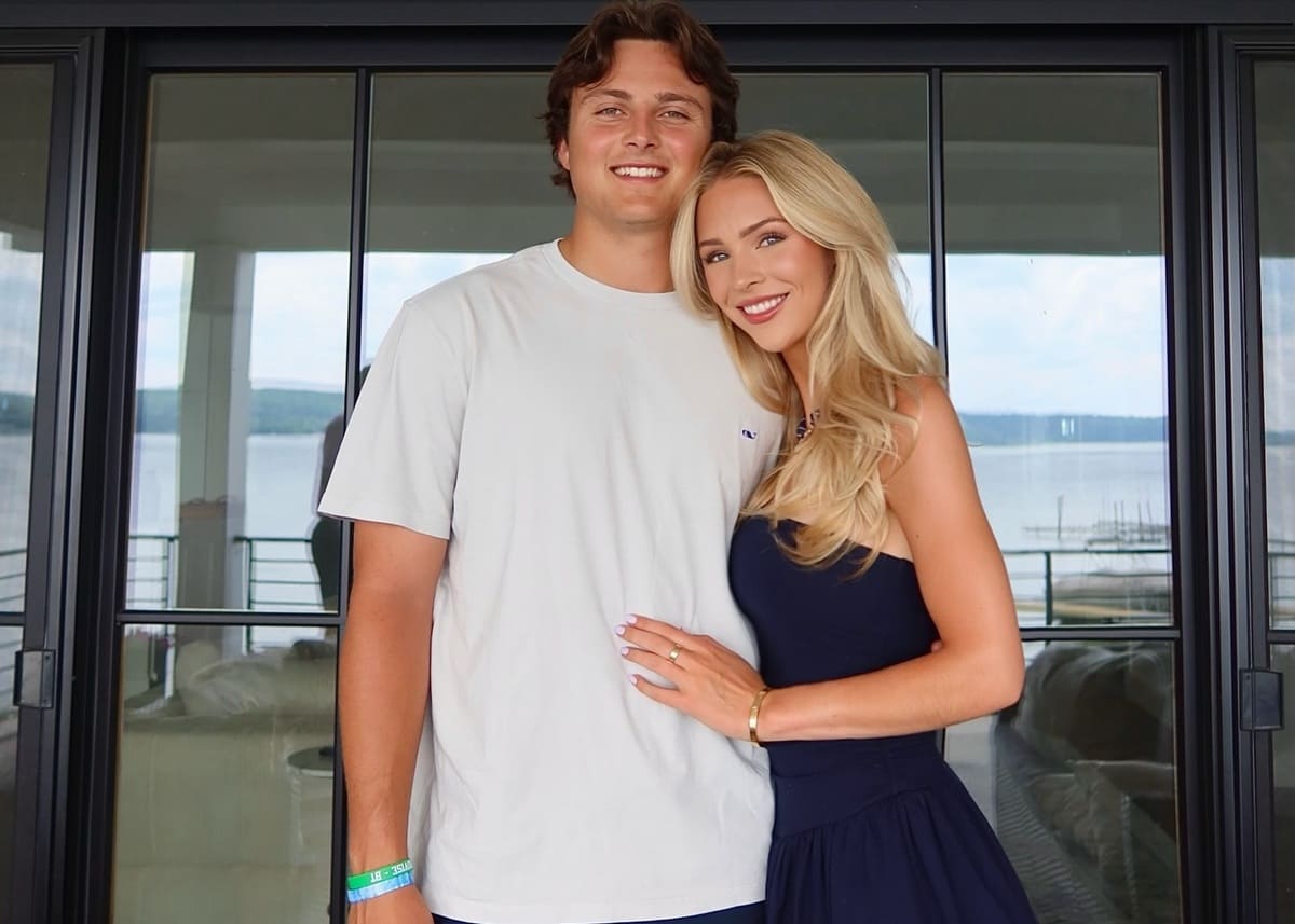 Young couple standing close together on a balcony with a sea view, smiling at the camera.