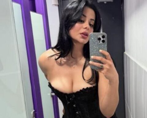 Woman in a black corset taking a mirror selfie, holding a glittery smartphone with one hand.