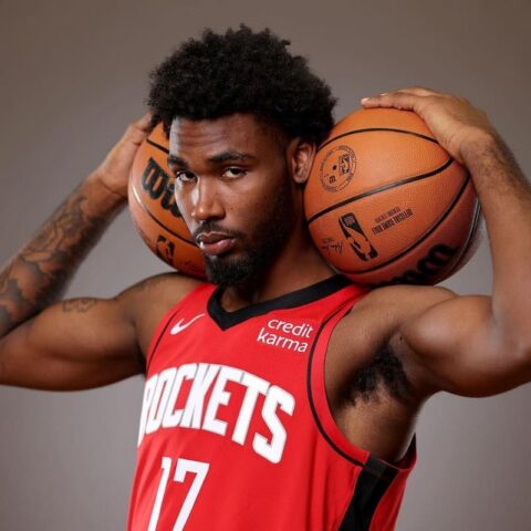 Basketball player in a red Rockets jersey (#17) holding two basketballs behind his head with both hands, looking at the camera.