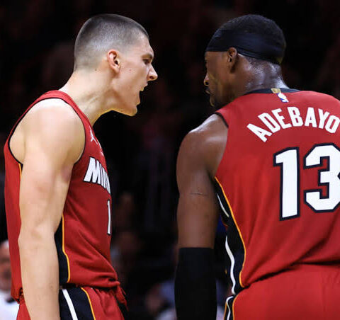 Two basketball players in red jerseys argue on the court during a game, with the number 13 visible on the back of one player's jersey.